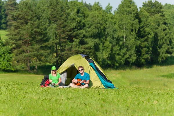 Junges Campingpaar kocht Mahlzeit und spielt Gitarre — Stockfoto