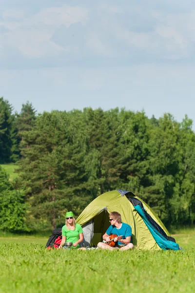 Junges Campingpaar kocht Mahlzeit und spielt Gitarre — Stockfoto