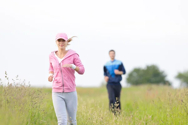 草原分野を実行している陽気な若いカップルをジョギング — ストック写真