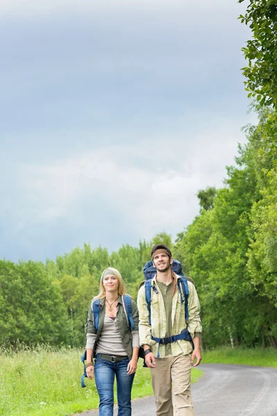 Caminhadas jovem casal mochila asfalto estrada campo — Fotografia de Stock