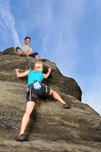 Kvinna klättring upp rock man hålla repet — Stockfoto