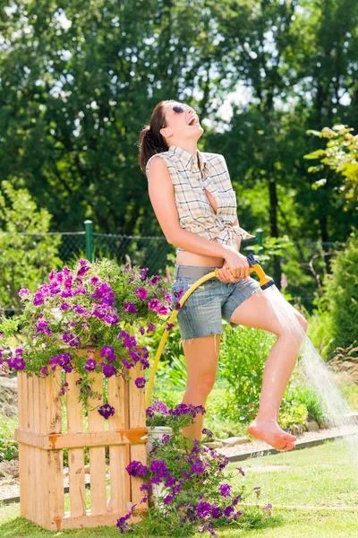 Летний сад, улыбающаяся женщина поливает траву из шланга — стоковое фото