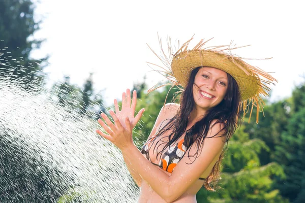 Letní zahrada usmívající se žena plavky stříkající vodě — Stock fotografie