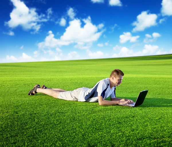 Молодой человек использует ноутбук на зеленом поле — стоковое фото
