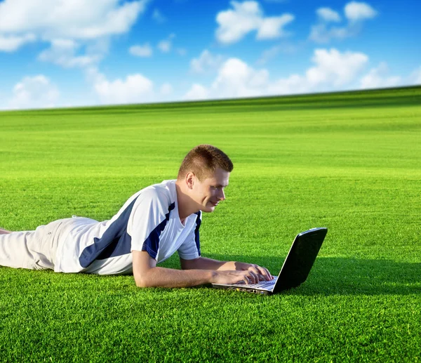 若い男は、緑の野原でノートブックを使用します。 — ストック写真