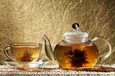 Glass teapot and a cup of green tea on a gold background clipart