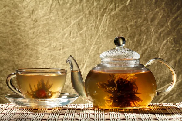 Glass teapot and a cup of green tea on a gold background — Stock Photo, Image