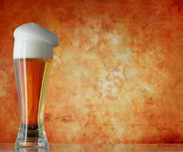 Glass of beer with froth over yellow background — Stock Photo, Image