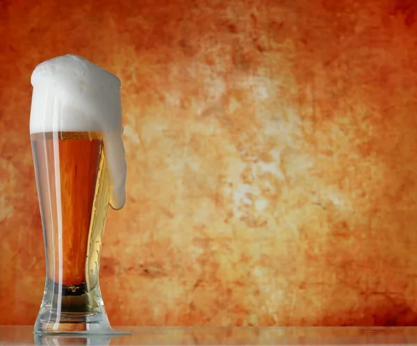 Glass of beer with froth over yellow background — Stock Photo, Image
