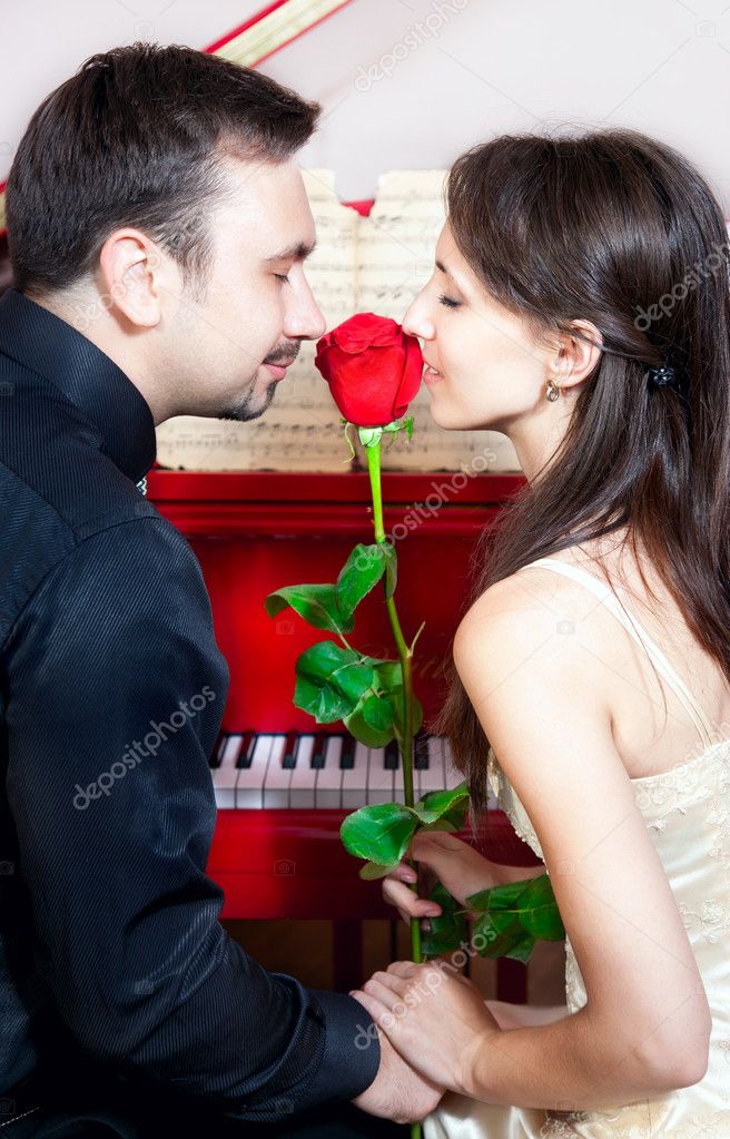 Couple smelling rose near red piano