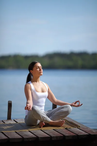 Chica entrena yoga en el muelle cerca del lago —  Fotos de Stock