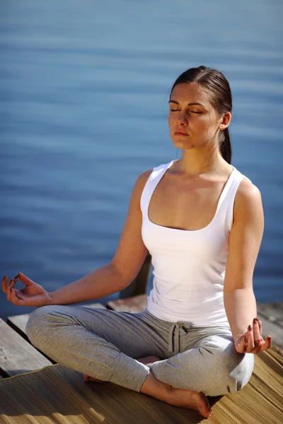 Chica entrena yoga en el muelle cerca del lago — Foto de Stock
