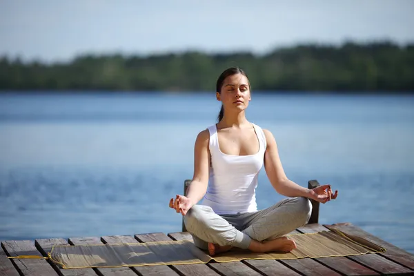 Flicka tränar yoga på bryggan nära lake — Stockfoto