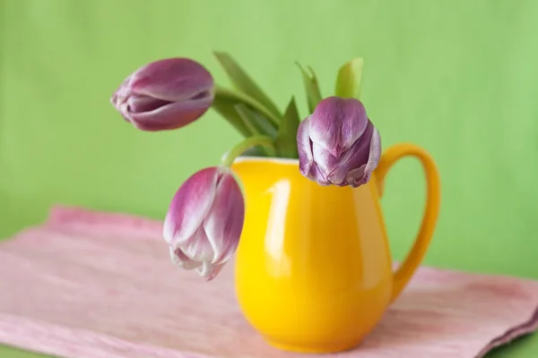Delicate bouquet of purple tulips in a yellow jug — Stock Photo, Image