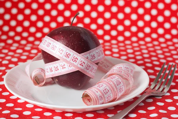 Červené jablko a měřicí pásky na bílé plotně — Stock fotografie