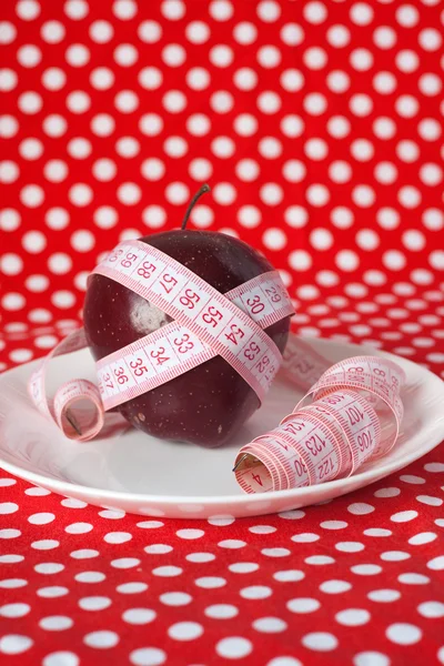 Red apple and measuring tape on a white plate — Stock Photo, Image