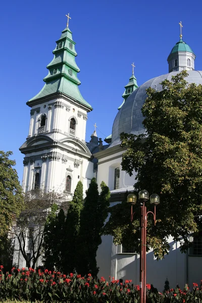 Vita kyrka med gröna kupoler och blomsterrabatter i stan — Stockfoto