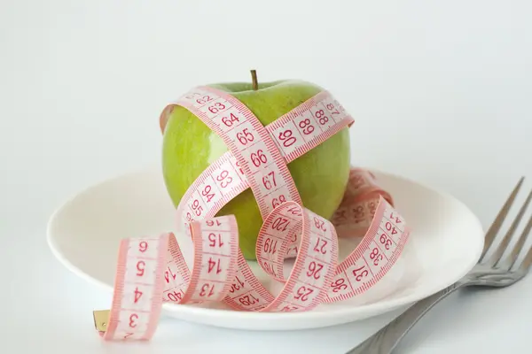 Зелене яблуко і мірна стрічка на білій тарілці і виделці — стокове фото