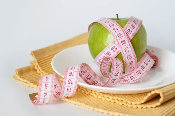 Zelené jablko a měřicí pásky na bílé plotně — Stock fotografie