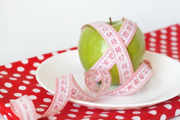 Zelené jablko a měřicí pásky na bílé plotně na tablec red polka dot — Stock fotografie