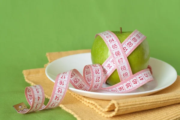 Manzana verde y cinta métrica en un plato blanco —  Fotos de Stock