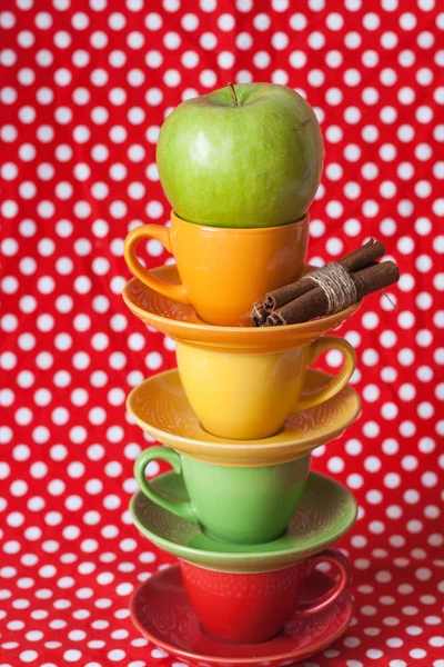 Grönt äpple, kanelstänger och ljusa koppar med röd bakgrund — Stockfoto