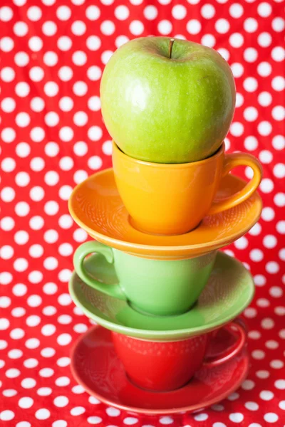 Green apple and bright cups with a red background — Stock Photo, Image