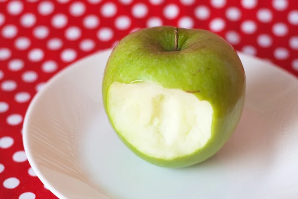 Manzana verde sobre un plato blanco sobre fondo rojo — Foto de Stock