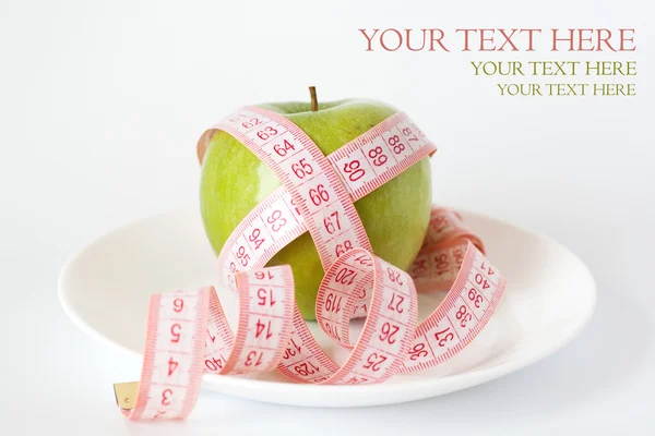 Green apple and measuring tape on a white plate — Stock Photo, Image