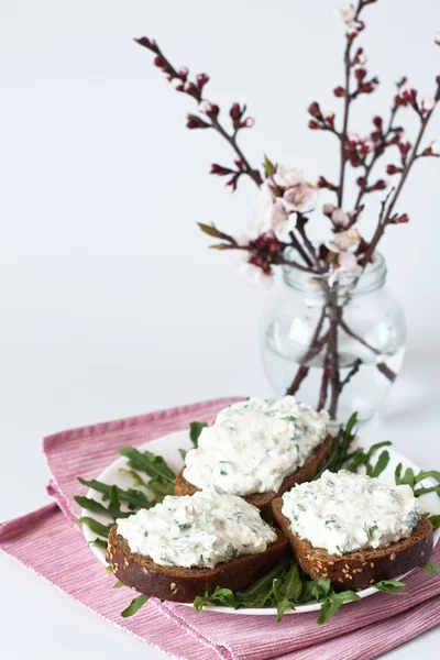 Сырные закуски на ржаном хлебе, руккола и букет цветущих вишневых ветвей — стоковое фото