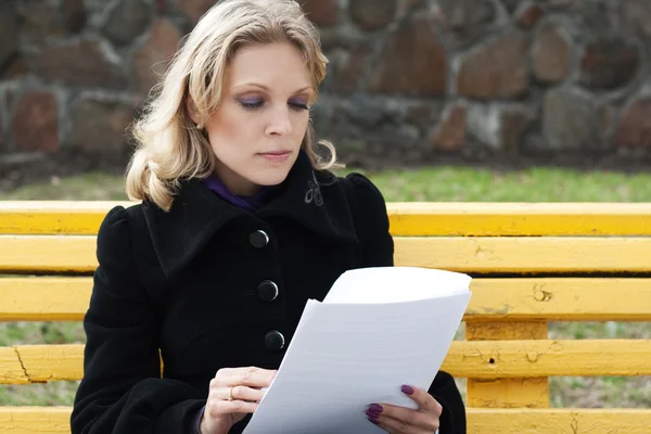 Giovane ragazza seduta su una panchina del parco e leggere il giornale — Foto Stock