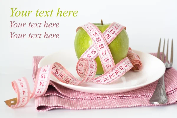 Green apple and measuring tape on a white plate and fork — Stock Photo, Image