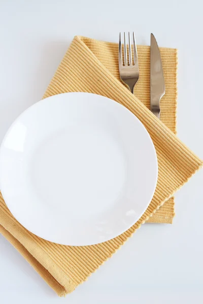 Tenedor, cuchillo, paño amarillo y plato blanco — Foto de Stock