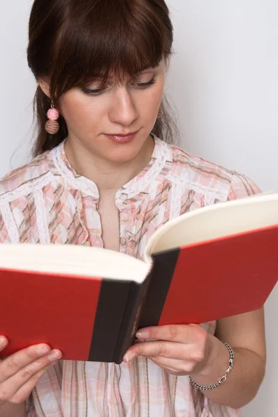 Sweet young brunette in a pink shirt reading book — Stock Photo, Image