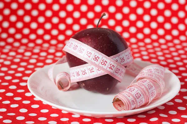 Červené jablko a měřicí pásky na bílé plotně — Stock fotografie