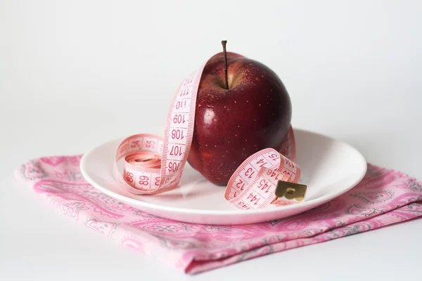 Červené šťavnaté jablko a měřicí pásky na bílé desce — Stock fotografie
