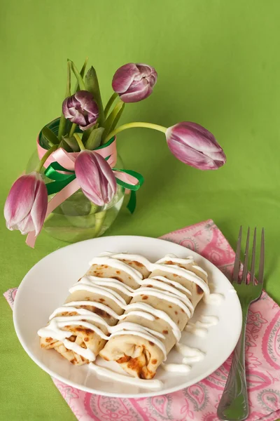 Panquecas com creme de leite para o pequeno-almoço e um vaso de tulipas roxas — Fotografia de Stock