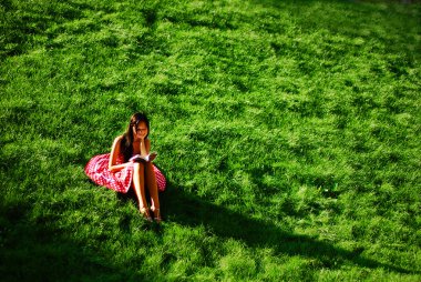 Girl with a book sitting on the grass clipart