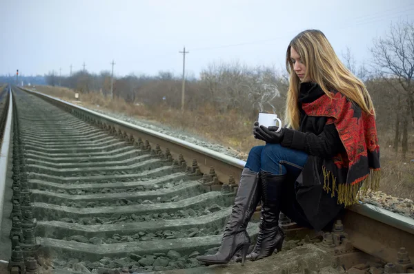 Dívka s šálkem sedí na kolejích — Stock fotografie