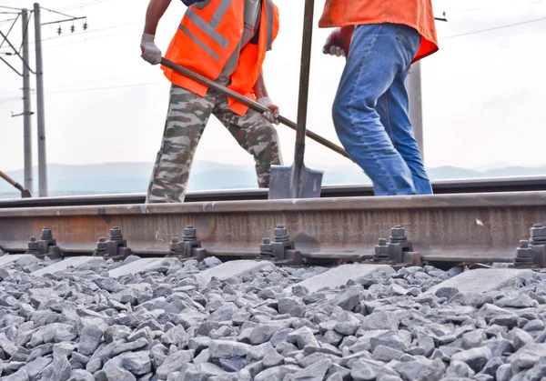 Železniční hráz, kolejnice a dělníci v oranžových vestách — Stock fotografie