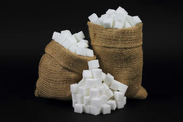 Cubos Açúcar em sacos de serapilheira sobre preto . — Fotografia de Stock