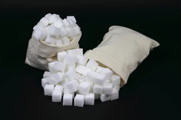 Gemorste kubussen suiker uit zakken over zwart. — Stockfoto
