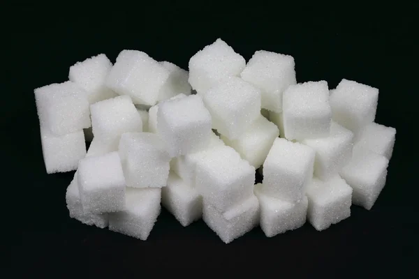 Cubos derramados Açúcar na pilha sobre preto . — Fotografia de Stock