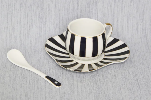 Una tazza a strisce su un piattino e un cucchiaio su uno sfondo grigio — Foto Stock