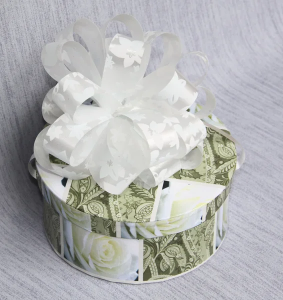 Un regalo in una scatola rotonda con un fiocco su sfondo grigio — Foto Stock