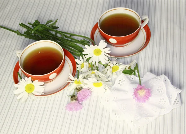 stock image Two red mugs with camomiles and pink wild flowers