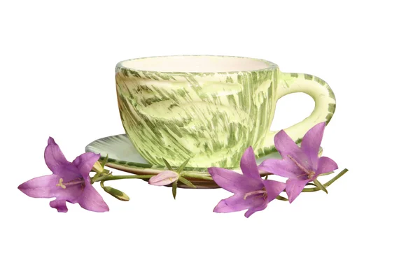 Una taza verde y campanas de mano lila sobre un fondo blanco — Foto de Stock