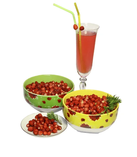 Des fraises sauvages dans des assiettes, une soucoupe et un verre de jus avec du tubul — Photo