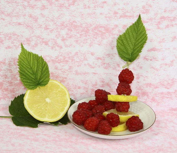 Uma framboesa com um limão em um pires em um fundo rosa — Fotografia de Stock