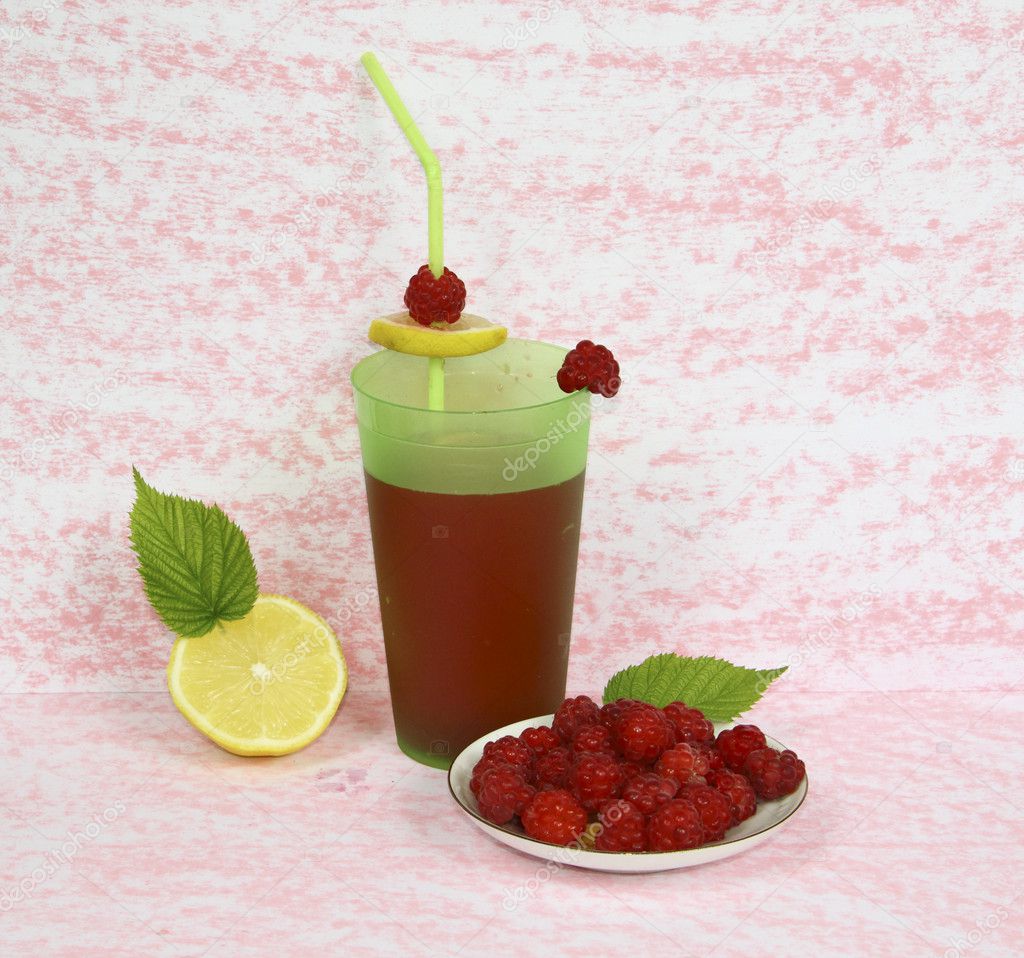 A raspberry on a saucer with a lemon and a juice glass on a pink background